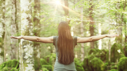Frau in balance von hinten zu sehen mit ausgebreiteten armen im wald